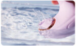 Close-up of a pink inflatable armband with a gold buckle on water as splashes rise nearby.