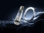 Futuristic handheld device with a transparent chamber and visible gears, beside a segmented silver ring on a rocky blue surface.