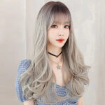 Portrait of a woman with long, wavy silver hair and bangs, wearing a blue gingham top and a star necklace.