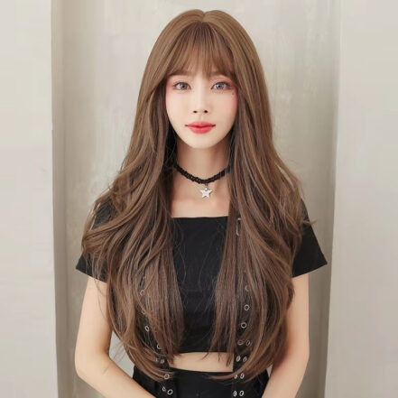 Portrait of a young woman with long wavy brown hair and bangs, wearing a black cropped top and a star pendant choker in front of a light background.