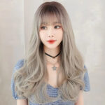 Portrait of a woman with long, wavy silver-gray hair and straight bangs, wearing a black choker and a star pendant necklace with a blue gingham top.