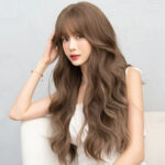Young woman with long, wavy light brown hair in a white sleeveless top, resting her head on her hand.