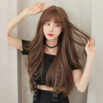 Portrait of a woman with long brown hair wearing a black crop top and choker, posing against a light background.