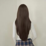 Person seen from behind with long straight brown hair reaching mid-back, wearing a white top and plaid skirt.