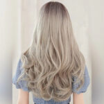 Back view of a person with long, wavy ash-blonde hair cascading over the shoulders, seen from behind.