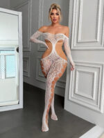 Woman posing in a pink lace off‑the‑shoulder bodysuit with cutouts, standing barefoot in a white paneled room and looking at the camera.