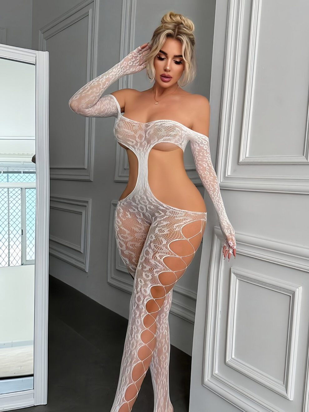 Woman in a sheer white lace off-shoulder bodysuit with thigh-high cutouts posing in a paneled room.