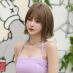 Young woman with a short light brown bob wearing a lavender halter top and choker, posing in a bright studio setting.