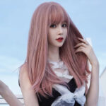 Portrait of a woman with long pink hair and bangs outdoors against a blue sky.