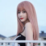 Portrait of a woman with long pink hair looking over her shoulder, wearing a black outfit, near a white railing outdoors.