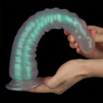 Glow-in-the-dark silicone curved dildo held between two hands, glowing teal against a black background.