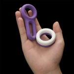Hand holding two purple silicone rings, one large loop with a vertical slot and a smaller white-and-purple ring, against a black background