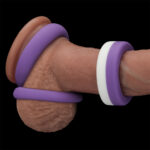 Close-up of a penis with multiple silicone cock rings in brown, purple, and white colors.