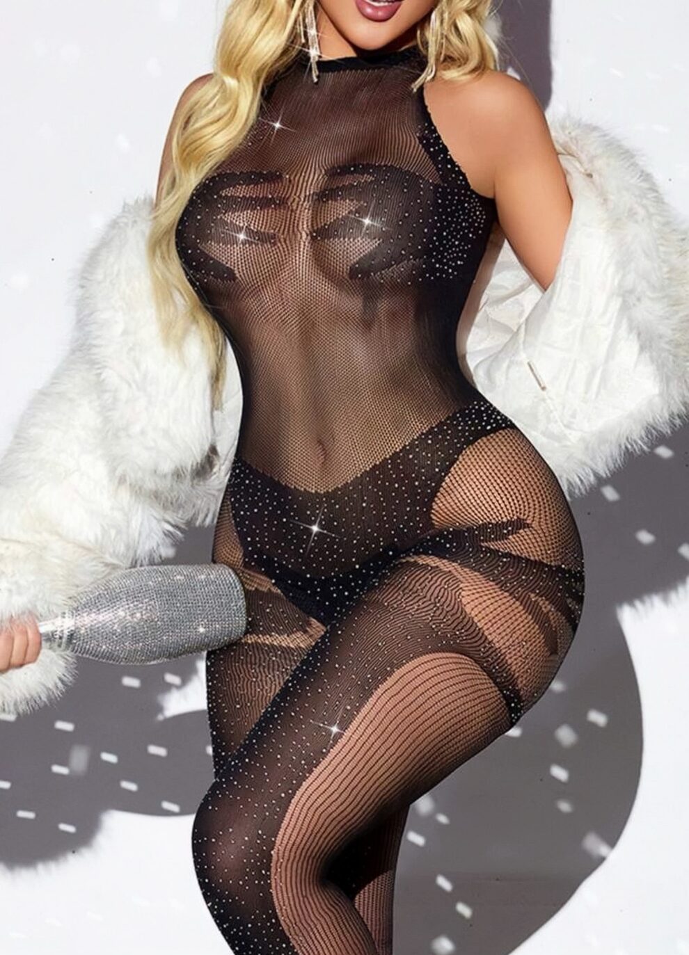 Model in a sheer black rhinestone mesh bodysuit with a white faux fur coat, holding a sparkly silver clutch.